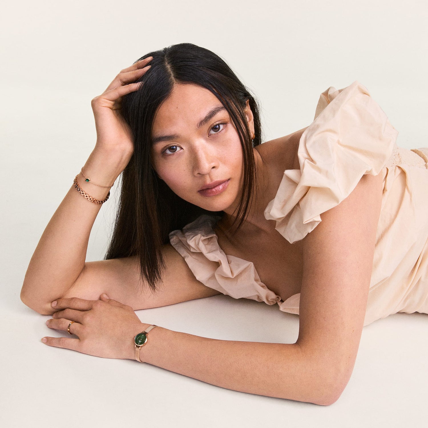 A woman wearing a cream ruffled dress showcases the May Charm S925 Sterling Silver with an emerald green crystal on a delicate bracelet, styled alongside other fine jewellery.