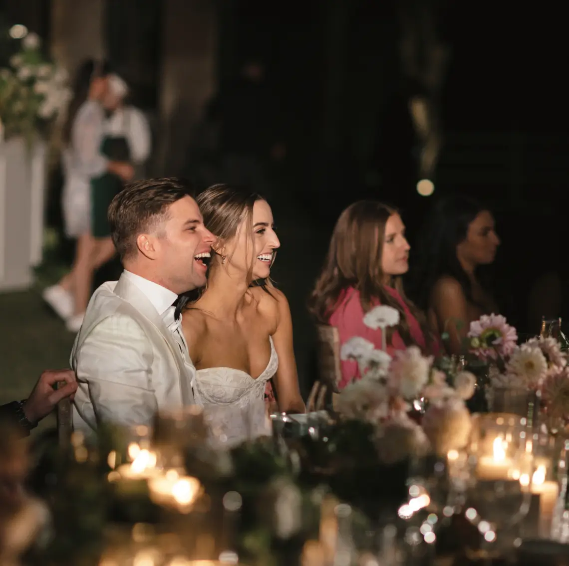 A joyful bride and groom in California share a candid laugh, surrounded by guests in a warm and intimate celebration. The image captures the genuine emotion and connection of a beautiful wedding moment catered by Chef Joann.