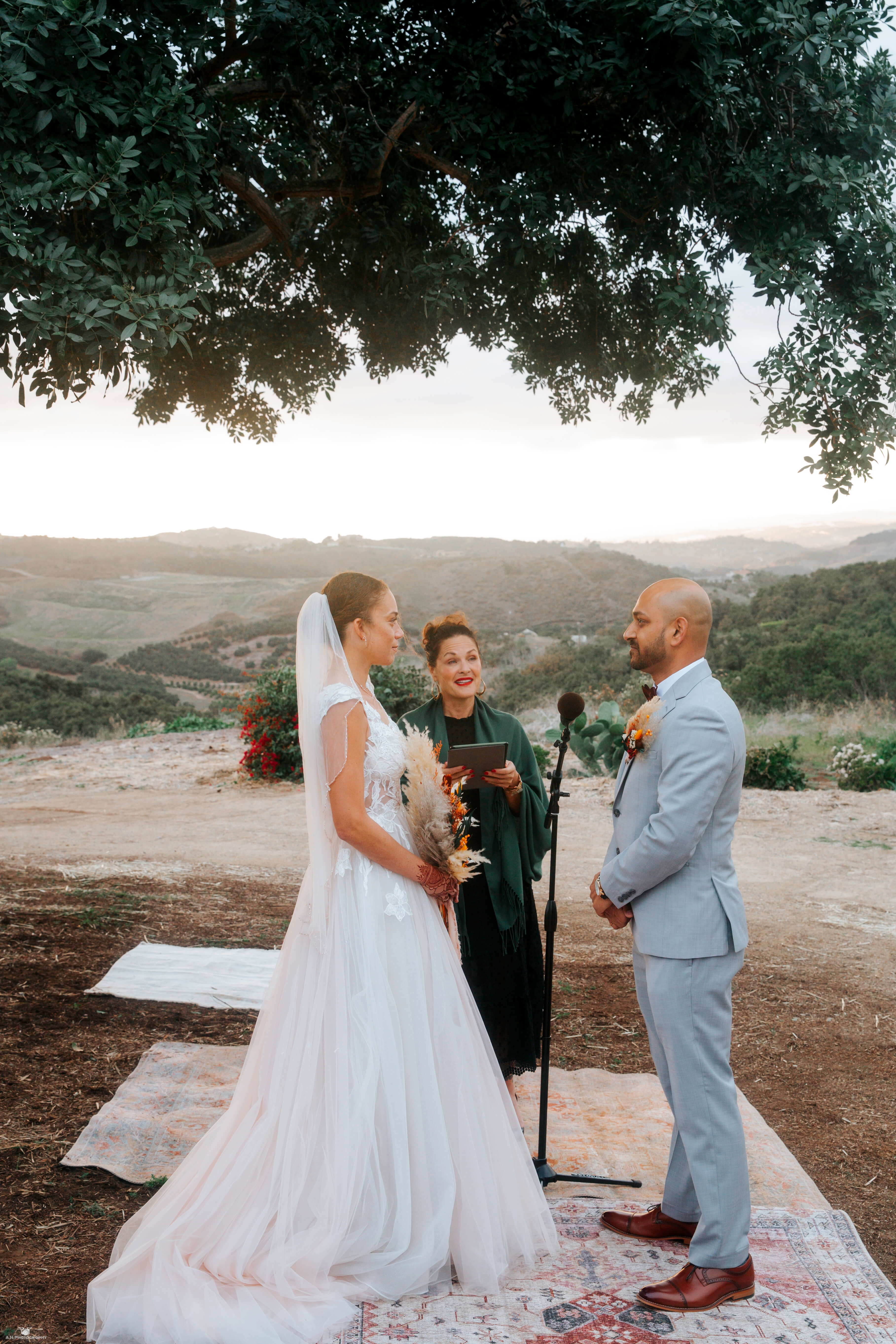 Bree & Yash sharing their first kiss as newlyweds under floral arches at Victoria Ranch, with Chef Joann Catering’s team preparing the reception feast.