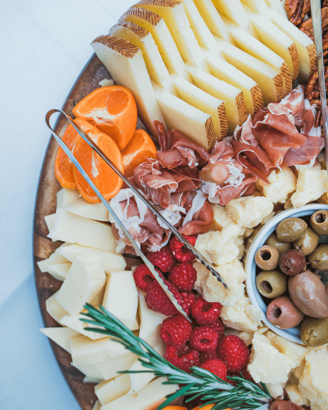 Close-up of gourmet appetizer plate featuring orange segments, rosemary, olive-cured bacon, and seasonal fruits, prepared by Chef Joann Catering.