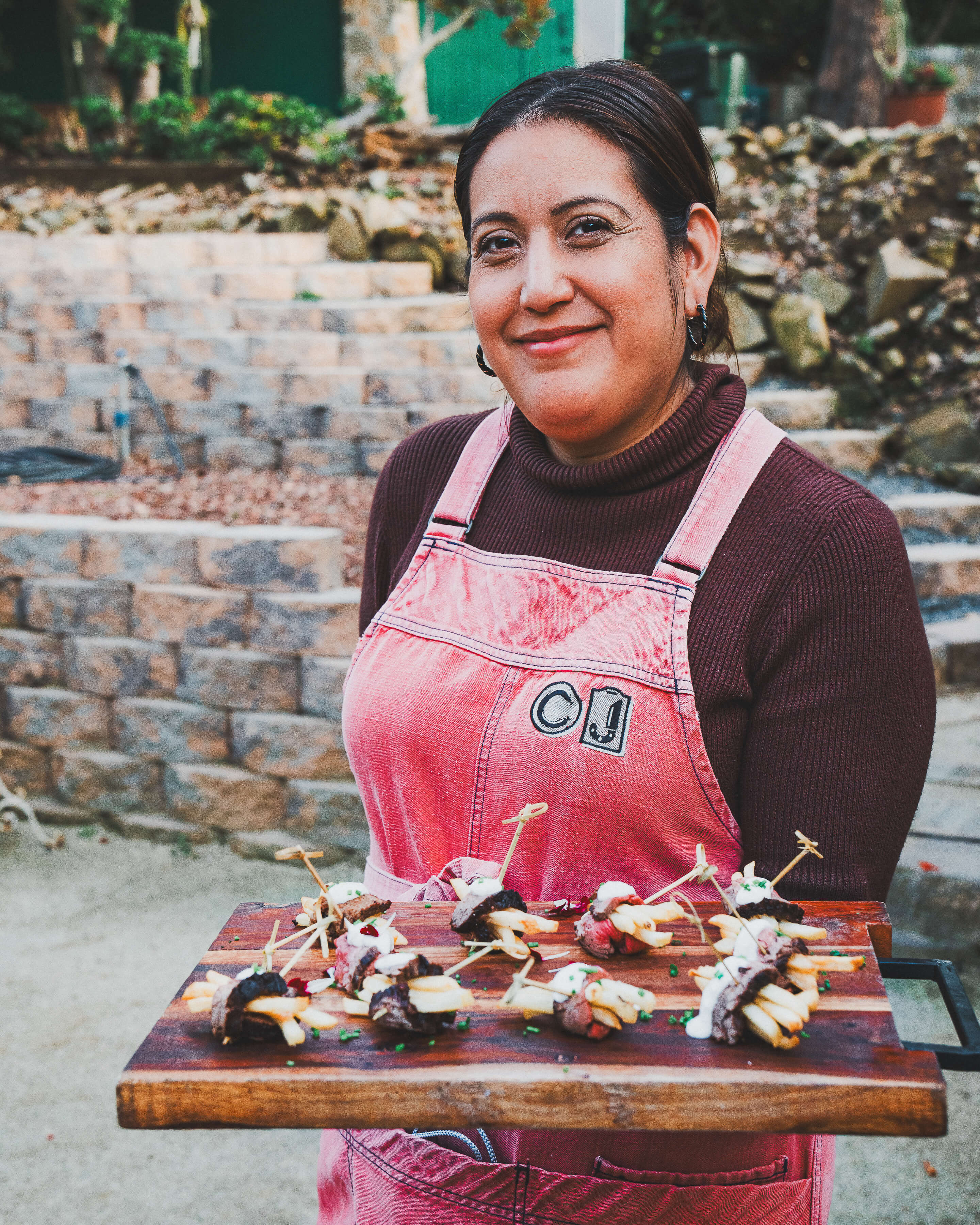 Chef Joann Catering team member in uniform presenting tray of French-inspired dishes at Julia Child tribute dinner, with Ala Mas wine pairings.