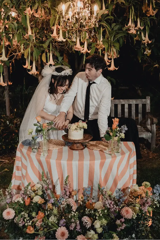 Bride and groom slicing their floral-decked cake in a Palm Springs garden oasis, curated by Chef Joann Catering’s culinary team.