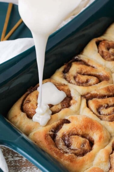The best cinnamon rolls glaze pouring over baked rolls.