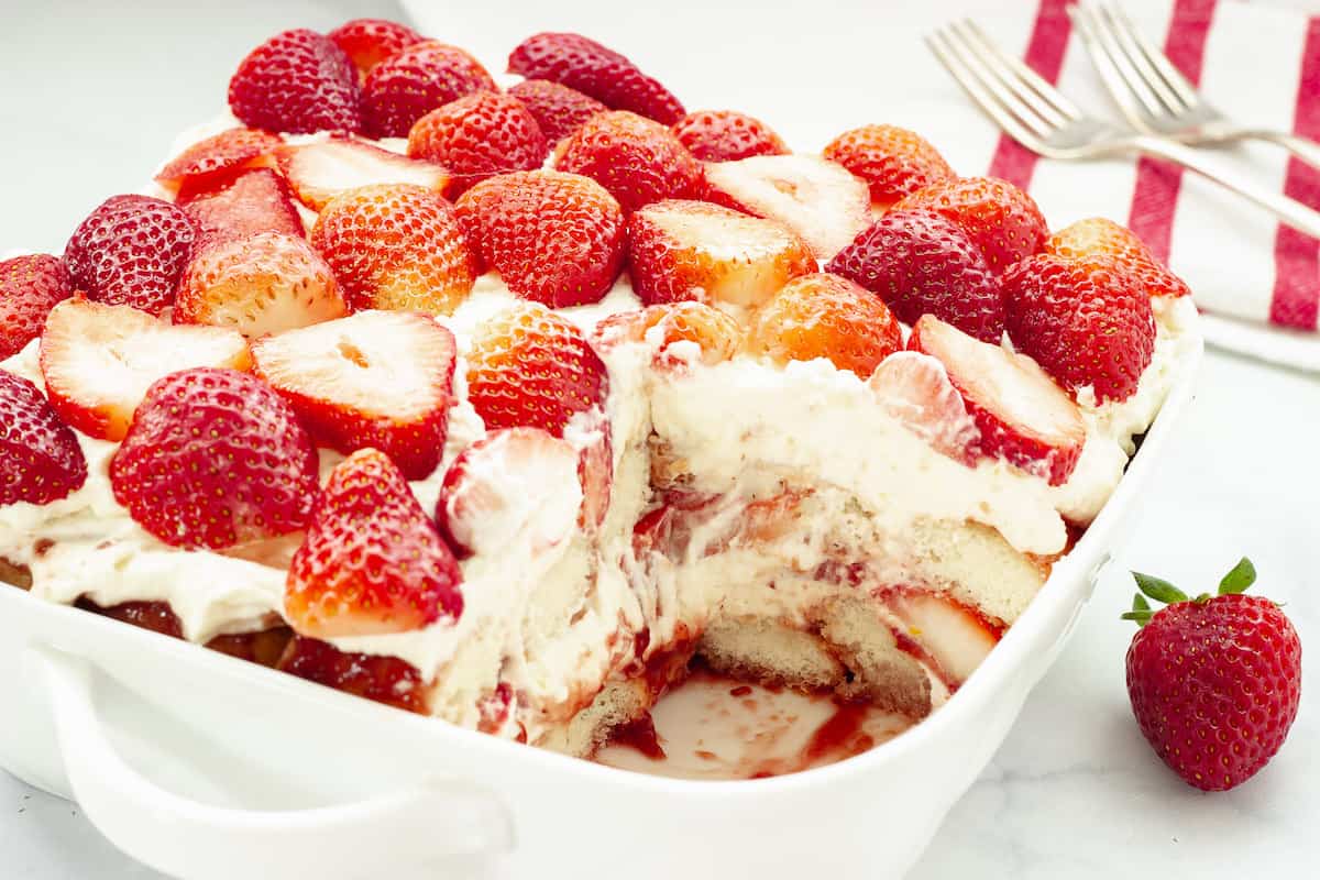 A white pan of strawberry tiramisu with one piece cut away.