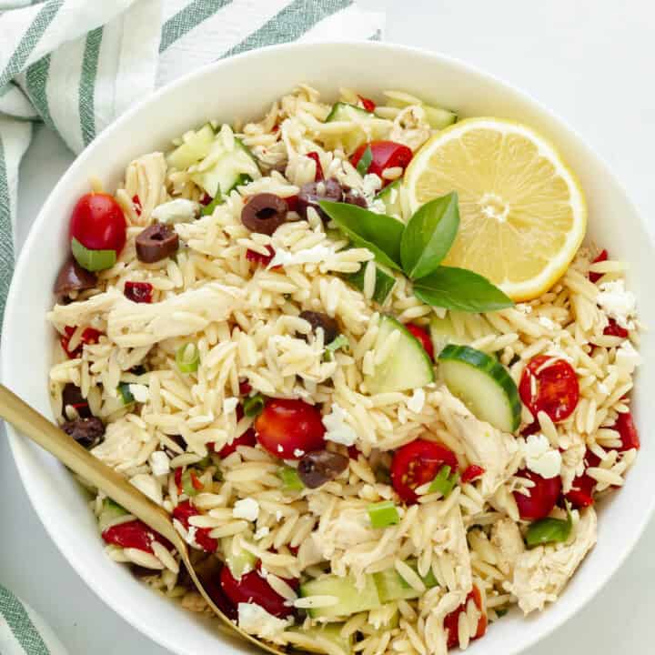 A white bowl with Greek chicken orzo salad next to a green and white striped napkin.