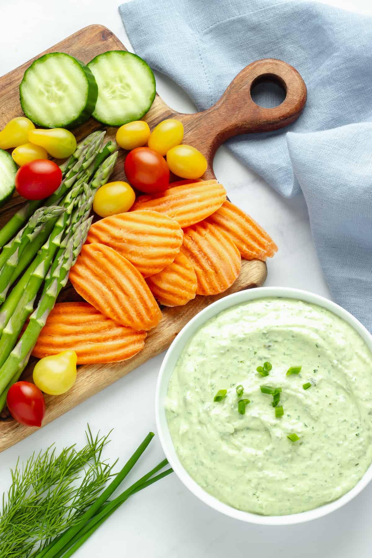 A bowl of green goddess dip next to a platter of vegetables.
