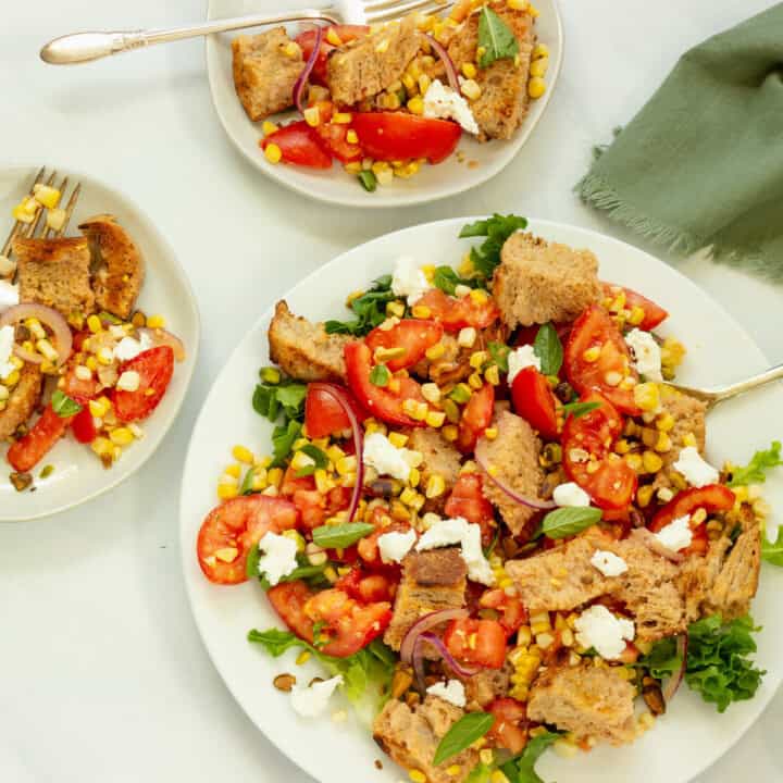 A white platter of corn and tomato salad with two smaller serving plates of the salad. A green napkin is in the background.