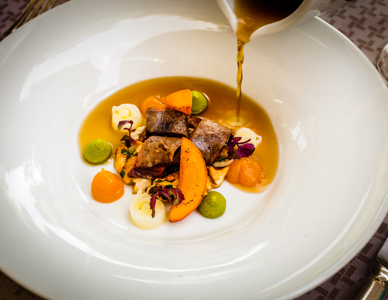 Eine Waldpilzboullion wird hier angegossen an rosa gebratenen Rehrücken, Pfifferlinge, Aprikosen und Lauch / © Foto: Georg Berg