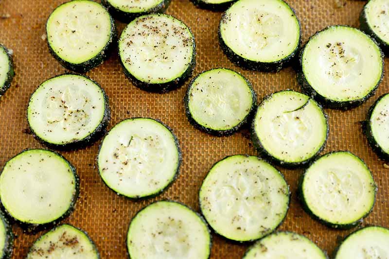 Horizontal image of roasted slices of seasoned squash on a baking sheet lined with a silicone mat.