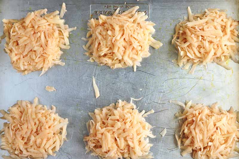 Horizontal image of mounds of shredded potato on an oiled baking sheet.