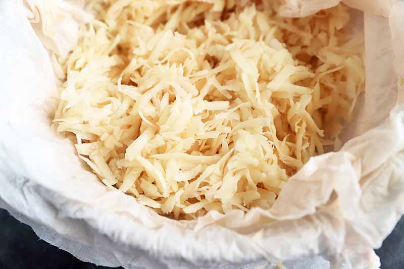 Horizontal image of dried grated potato in a towel-lined bowl.