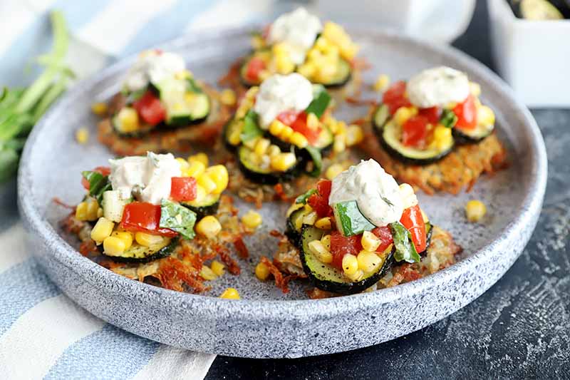 Horizontal image of a round gray plate with individual savory potato pancakes topped with assorted vegetables and yogurt.