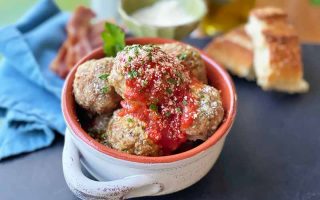 Horizontal image of a dish filled with individual ground turkey mounds covered in marinara next to a blue towel and bread.