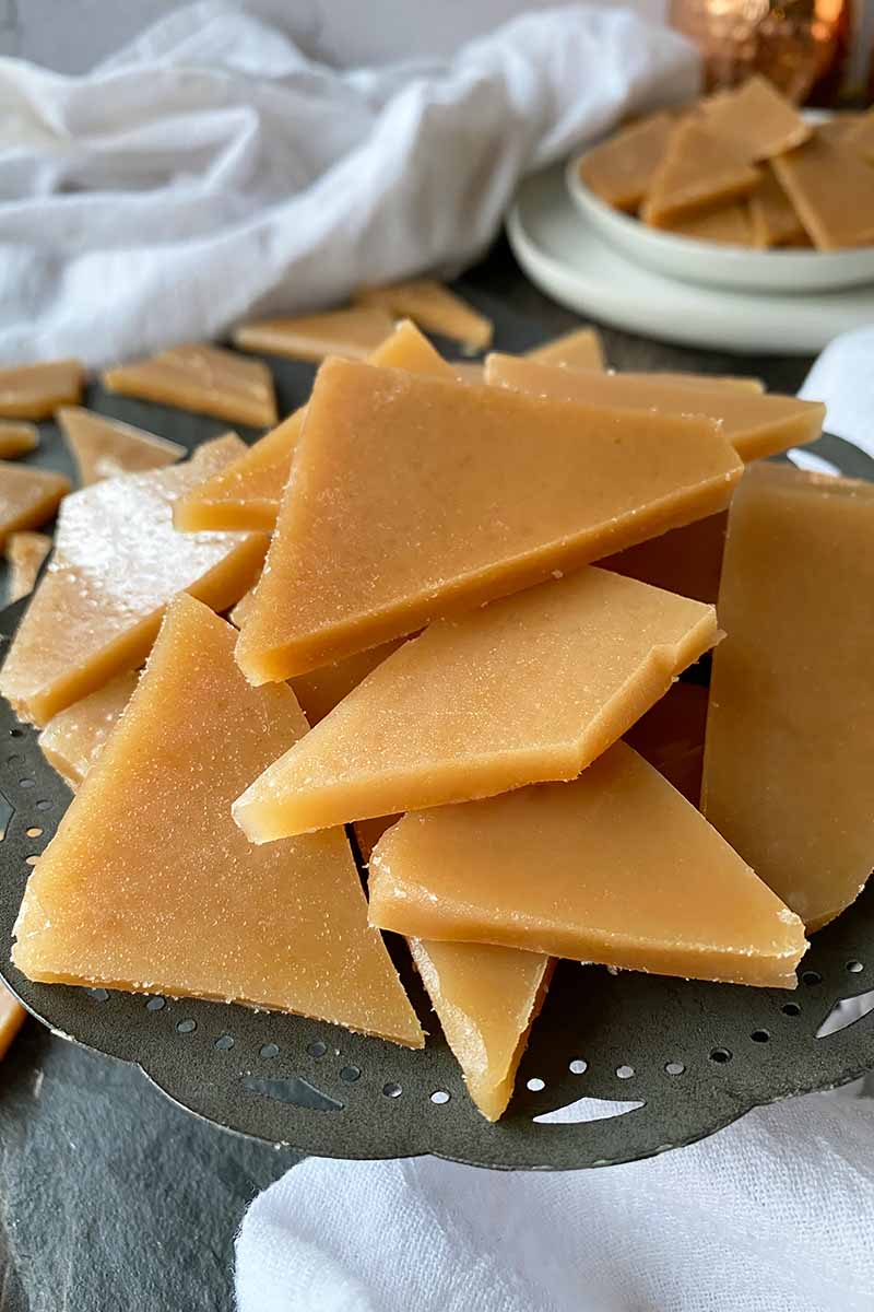 Vertical image of piles of hard caramel pieces on a gray stand and white plates.