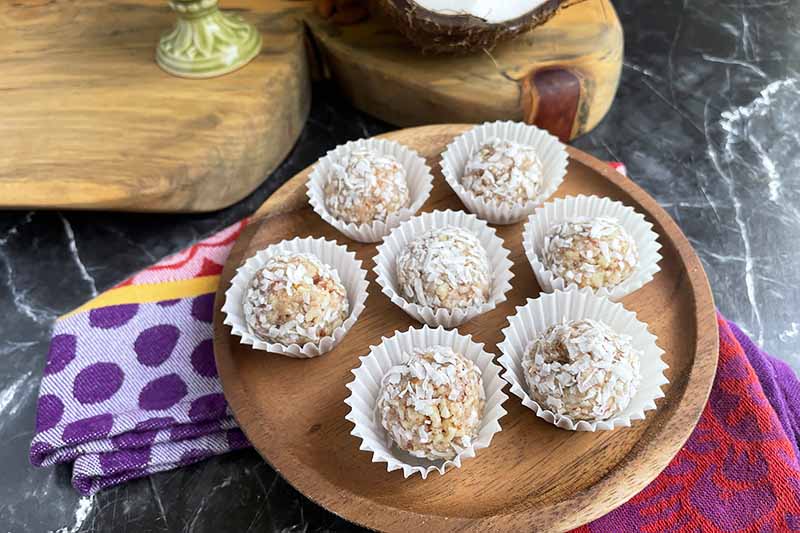 Horizontal image of snack balls in white muffin liners on a white plate on top of a colorful napkin.