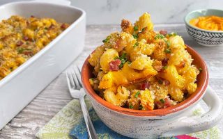 Horizontal image of a small bowlful next to a large white casserole dish of macaroni and cheese.