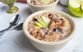 Horizontal image of two white bowls filled with a creamy porridge topped with fresh fruit next to spoons.