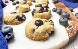 Horizontal image of rows of individual baked treats topped with fresh fruit on a marble surface next to blue towels.