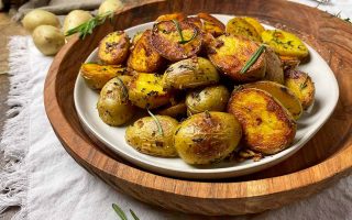 Horizontal image of a plateful of browned baby golds with fresh herbs on top of a wooden serving tray.