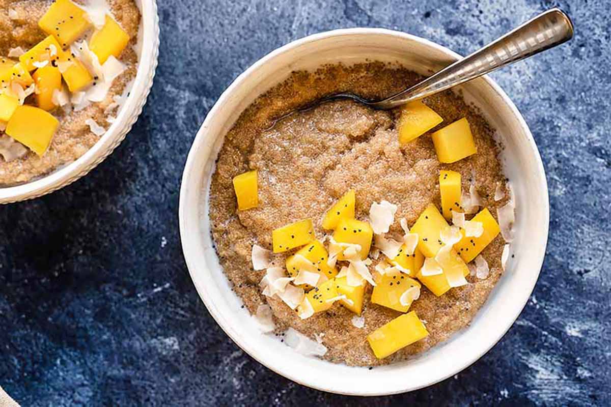 Horizontal image of amaranth porridge in bowls garnished with cubed mango and shredded coconut.