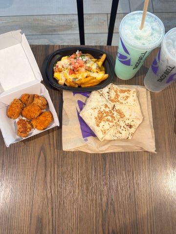 Fast food meal featuring chicken bites, loaded fries, burritos, and drinks.