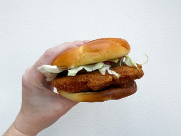 A hand holding a fried chicken sandwich with lettuce in a bun A hand holding a fried chicken sandwich with lettuce in a bun