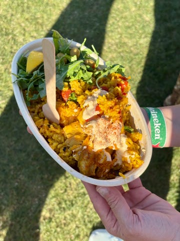 A bowl of colorful rice dish with greens and a wooden spoon.