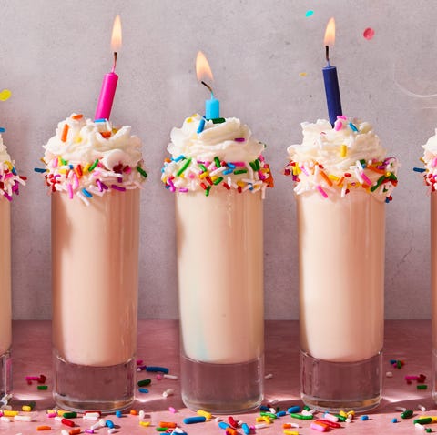Birthday Cake Shots shot in a shot glass topped with sprinkles, whipped cream, and a candle