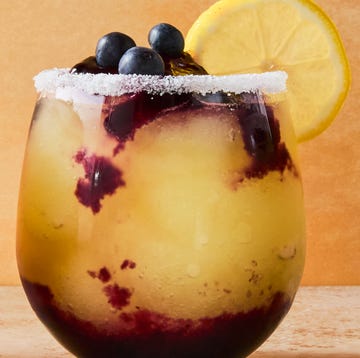 Frozen Blueberry Lemon Drop Slushies stemless glasses filled with a frozen vodka lemon cocktail with a blueberry syrup swirled in the glass. garnished with a sugared rim, lemon wheels, and fresh blueberries