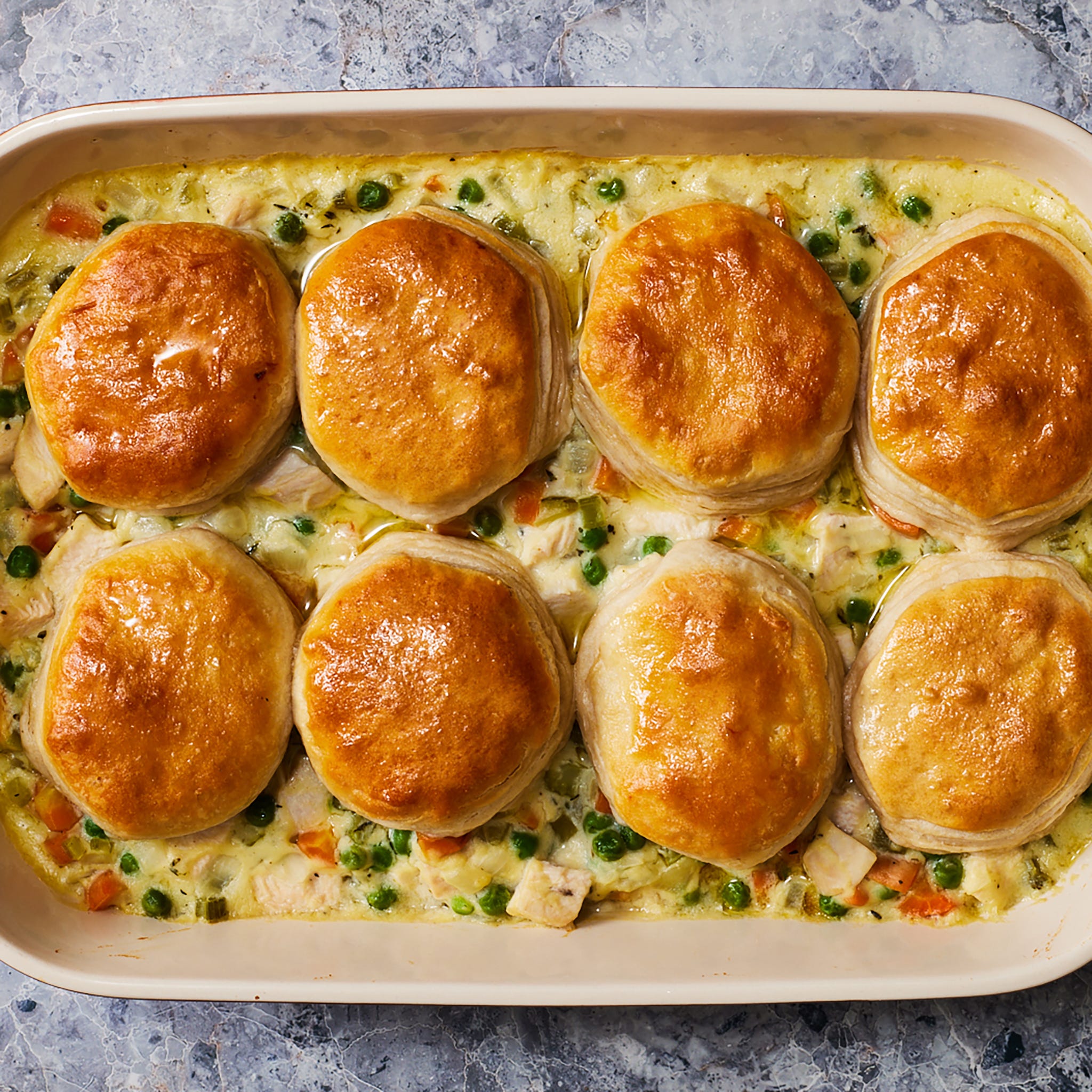 chicken pot pie filling in a casserole dish topped with biscuits
