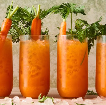 Carrot Margaritas orange carrot margaritas in a tall glass with carrots and carrot stems as garnish