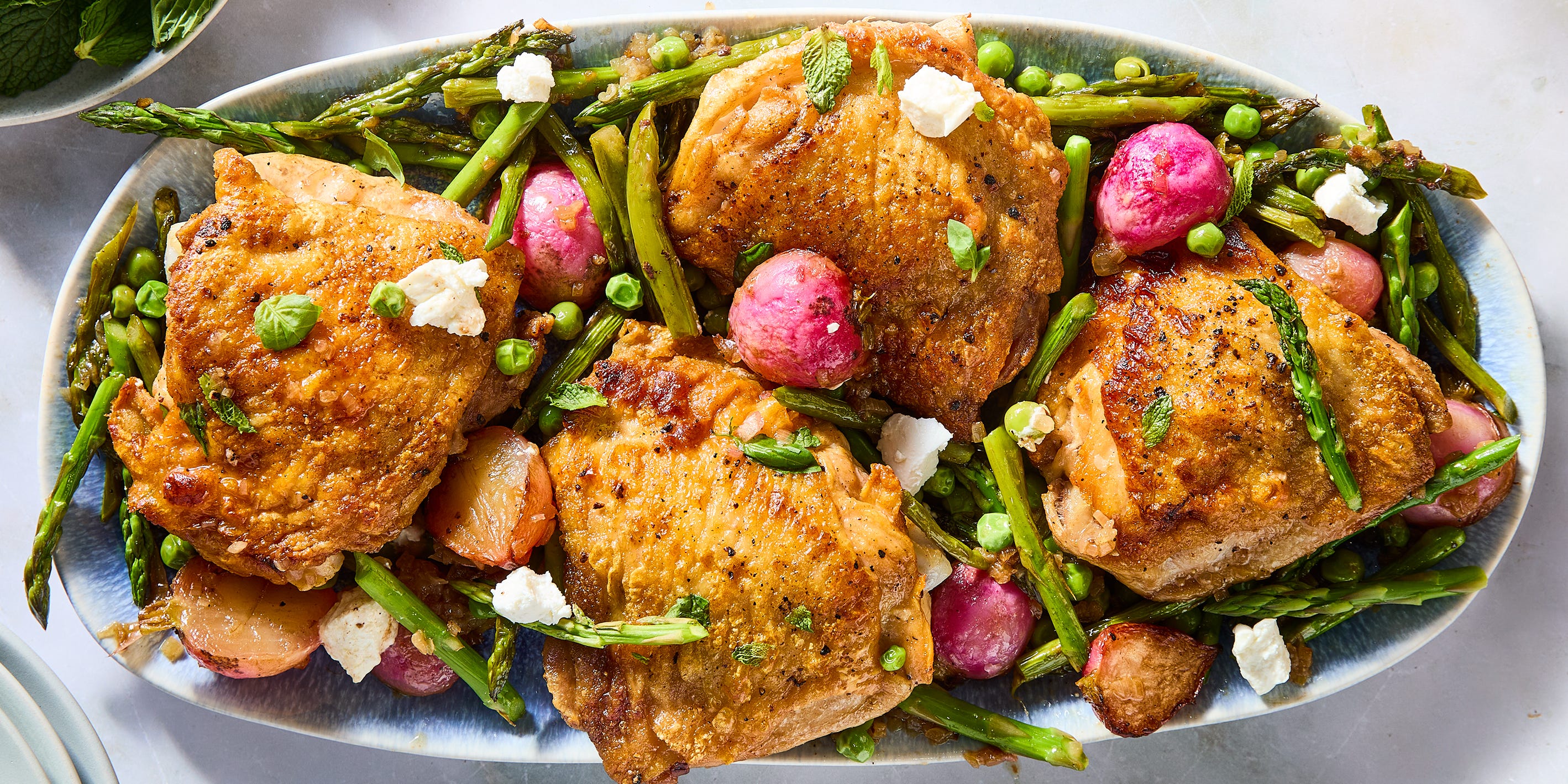 One-Pan crispy chicken primavera crispy chicken thighs with roasted radishes, asparagus, and peas on a white platter