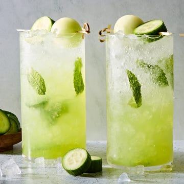 Cucumber Melon Mojito a glass filled with ice, rum, mint leaves, midori liqueur, and lime juice garnished with a cucumber slice and honeydew melon ball