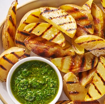 Grilled potatoes grilled potatoes on a white platter with a bowl of green herb sauce