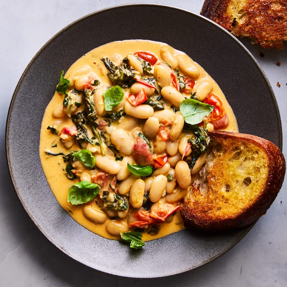 Creamy tuscan white bean skillet creamy tuscan white beans on a grey plate topped with basil, with toast alongside