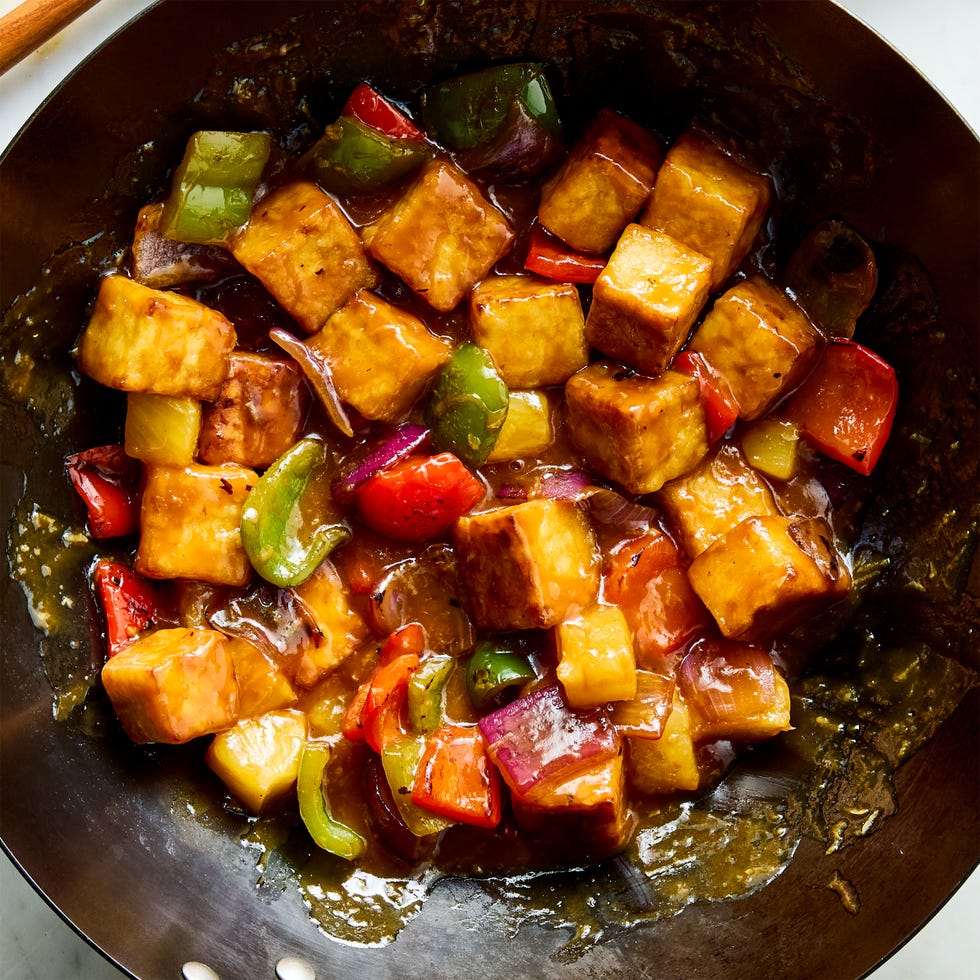 a pan of crispy tofu cubes with red onion, bell peppers, pineapple, and a sweet and sour sauce