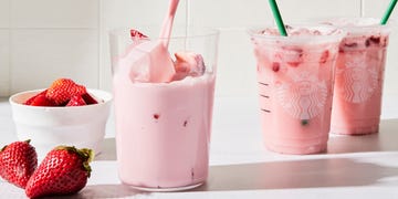 a tall glass filled with a creamy light pink beverage, ice, and sliced fresh strawberries