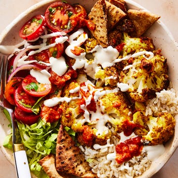 Halal Cart-Style Cauliflower Bowl roasted cauliflower in a bowl with tomato salad, crushed pita, onions on top of rice and drizzled with white halal cart style sauce