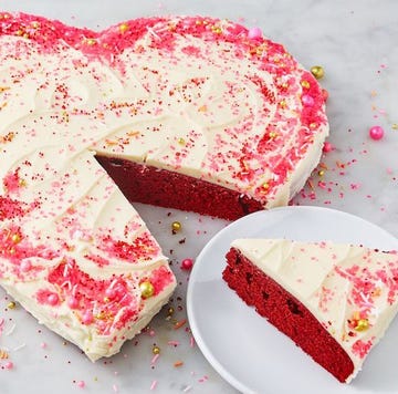 Heart Shaped Cake heart shaped red velvet cake covered in icing and sprinkles with a slice taken out of it on a plate