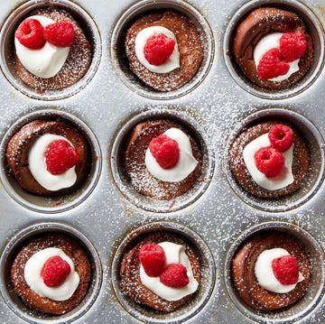 Mini Chocolate Dutch Baby Pancakes miniature chocolate flavored dutch baby pancakes sitting in the wells of a muffin tin and garnished with whipped cream, raspberries, and powdered sugar