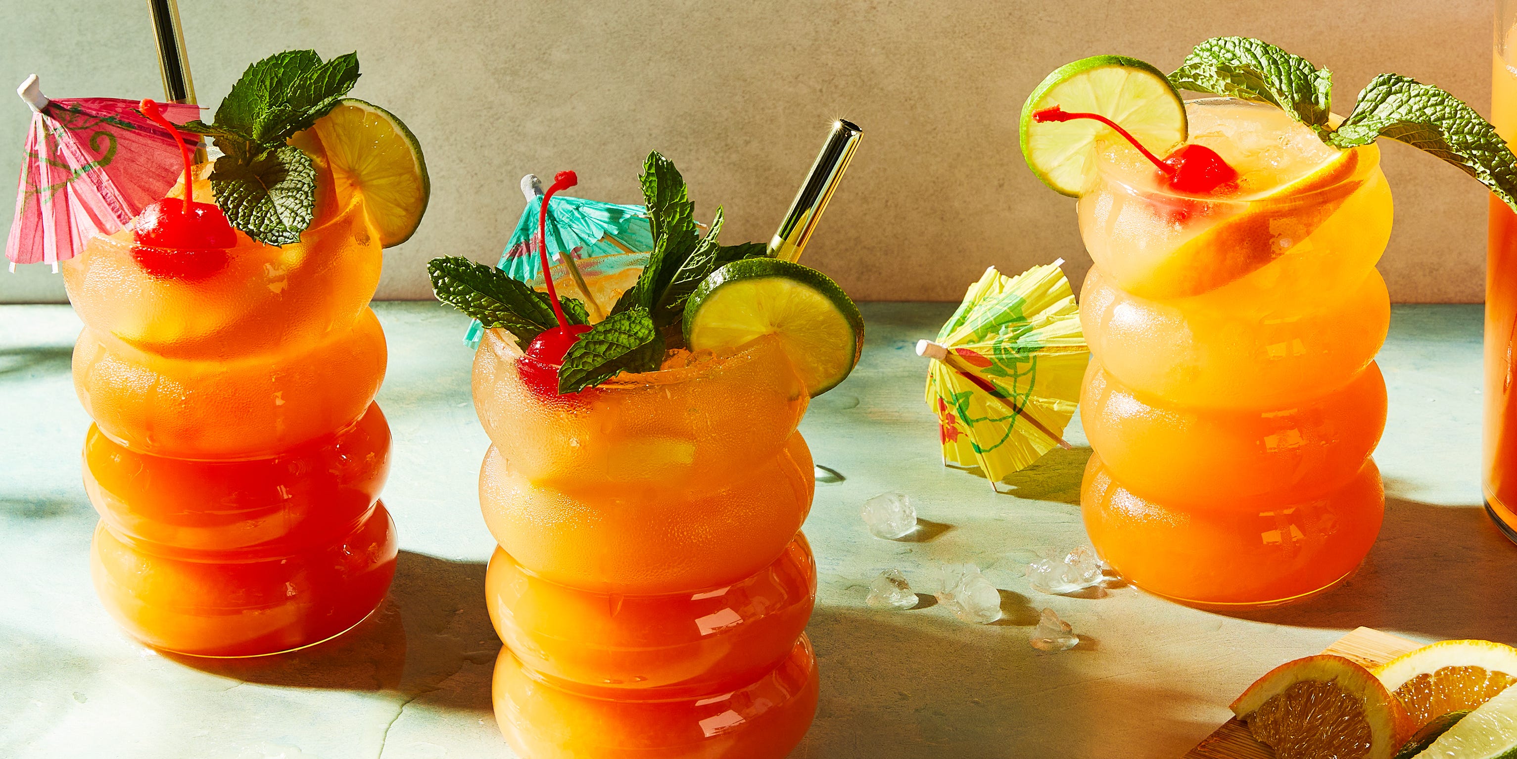 Rum Punch rum punch cocktail in a glass with mint, an orange slice, a lime wheel, and a maraschino cherry