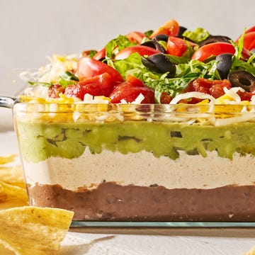 Seven Layer Dip layered dip with refried beans, sour cream, guacamole, cheese, tomatoes black olives, and lettuce in a clear dish
