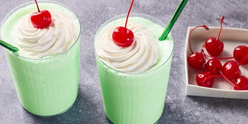 green shake in a glass with whipped cream, a cherry, and a green straw