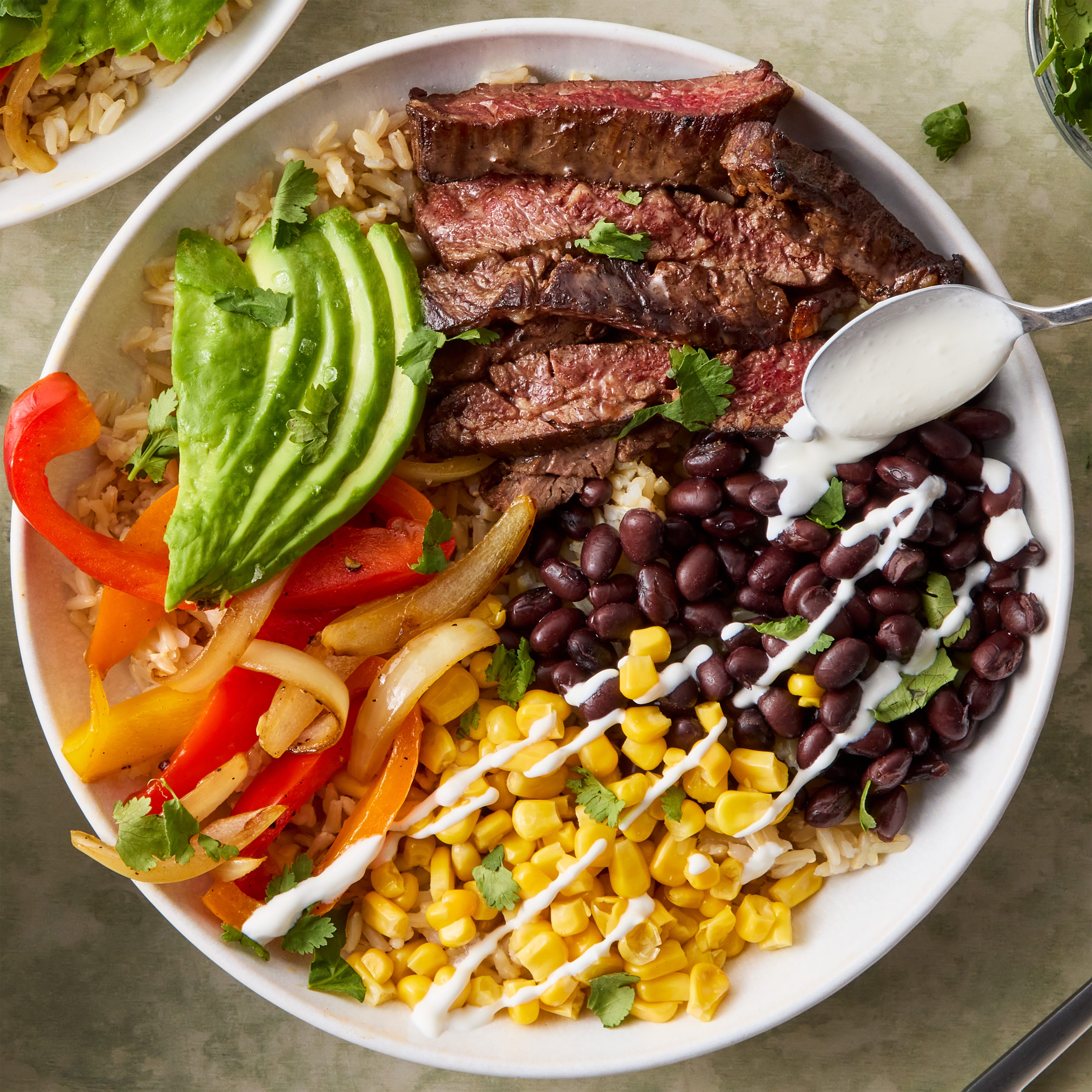 sliced steak with grilled peppers, corn, avocado, and black beans over rice