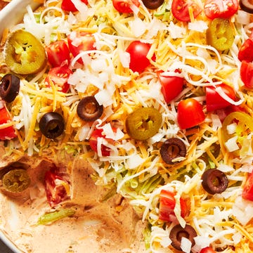 Taco Dip layered dip with sour cream, shredded lettuce, shredded cheese, black olives, tomatoes and jalapenos