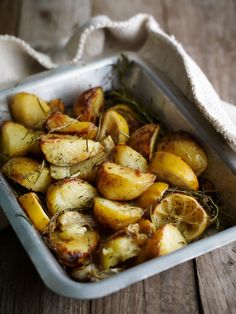 a pan filled with potatoes and herbs on top of a wooden table next to a towel
