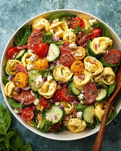 a white bowl filled with pasta salad and topped with tomatoes, cucumbers, spinach