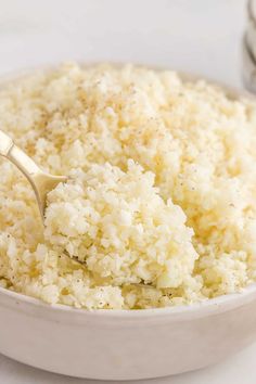 a white bowl filled with rice on top of a counter next to a silver spoon