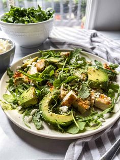 a white plate topped with avocado salad next to a bowl of feta cheese