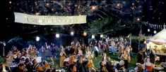 a large group of people standing around a tent at night with lights in the background